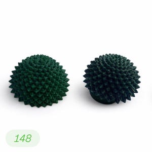 May include: Two dark green, spiky, spherical objects, possibly decorative items or sculptures, are displayed against a white background. The objects have a textured surface with numerous small, pointed protrusions. The number "148" is visible in a green oval.