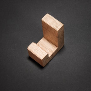 May include: A wooden, L-shaped object with a natural wood grain finish. The object is a light brown color and appears to be a small shelf or hook. The item is positioned on a dark gray surface.