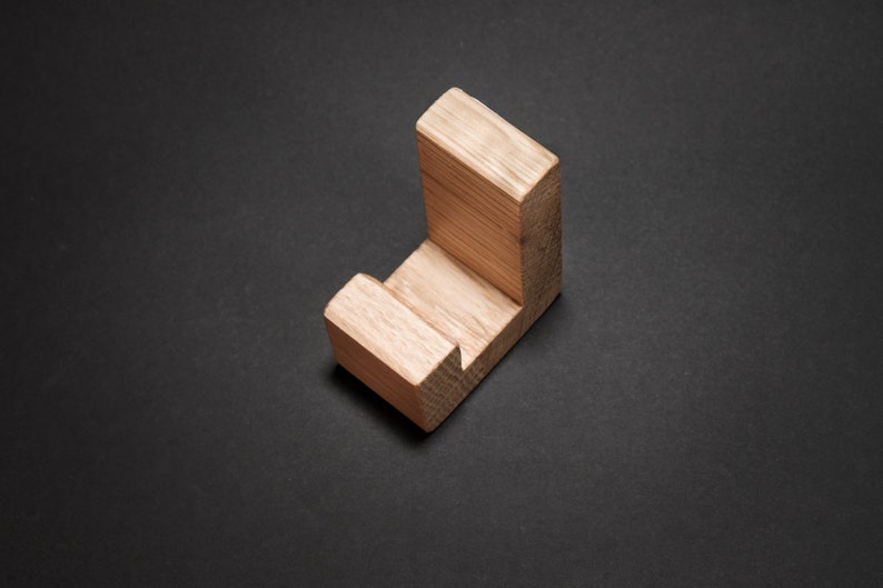 May include: A wooden, L-shaped object with a natural wood grain finish. The object is a light brown color and appears to be a small shelf or hook. The item is positioned on a dark gray surface.