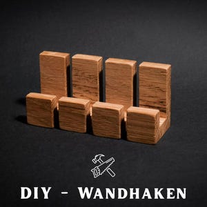 May include: Four L-shaped wooden wall hooks arranged in a row. Each hook features a vertical back piece and a shorter horizontal front piece, showcasing a natural wood grain texture. Below the hooks, the text reads DIY - WANDHAKEN.