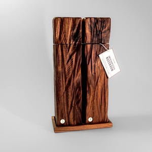 Op de afbeelding: Een hoge, rechthoekige houten sculptuur met een textuur die op schors lijkt. Het donkerbruine hout is gemonteerd op een kleine, rechthoekige basis. Een label is bevestigd met de tekst "SCHWEIZERISCHER NUSSBAUM".