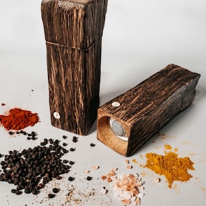 May include: Two wooden spice grinders with a rustic finish. The grinders are filled with different spices, including black peppercorns, paprika, turmeric, and pink Himalayan salt.