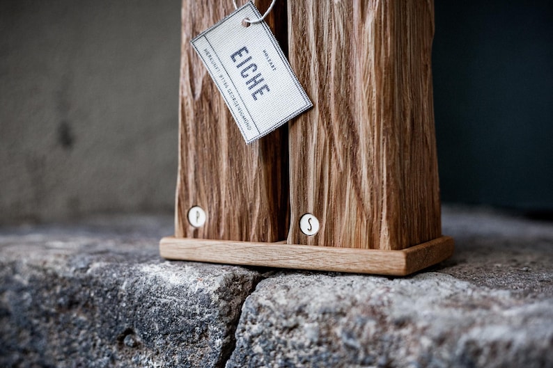 May include: Wooden salt and pepper shakers with a textured surface. The shakers are made of light brown wood and have a small tag that says "EICHE". The shakers are labeled with "P" and "S" on the front.
