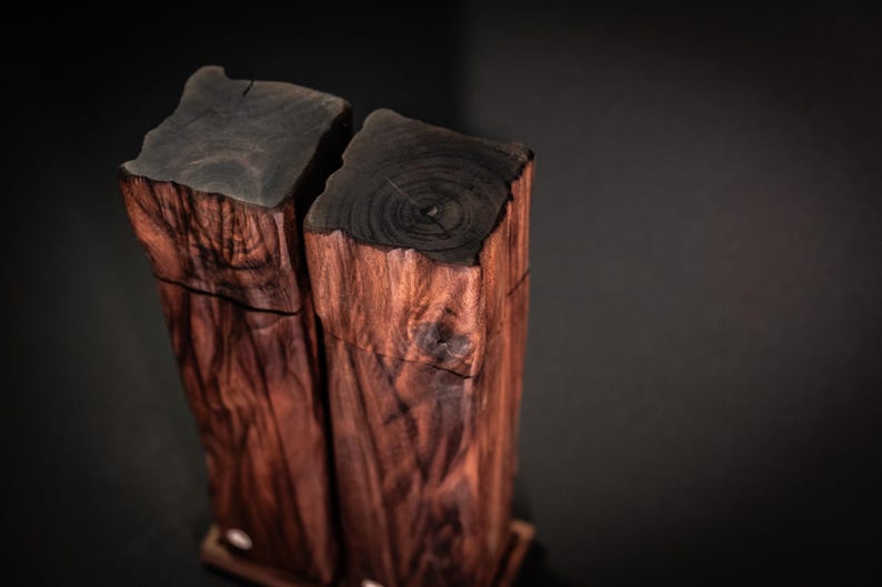 Op de afbeelding: Twee houten blokken met een donkere, getextureerde bovenkant en een rijke, roodbruine nerf. De blokken zijn rechthoekig en staan rechtop, waarbij de natuurlijke houtpatronen worden getoond. De achtergrond is donkergrijs.