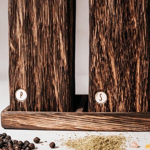 May include: Two dark brown wooden salt and pepper shakers with a white base. The shakers have a white label with the letters "P" and "S" on them.