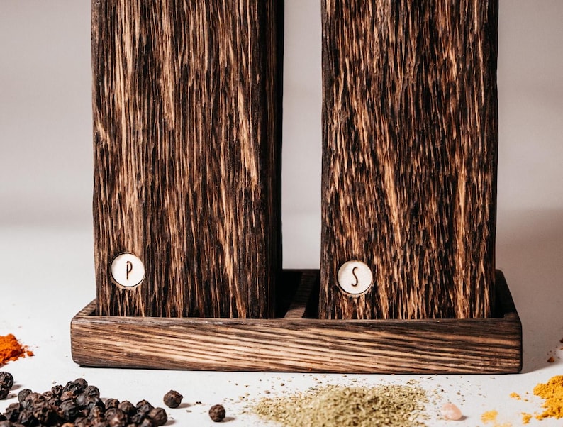 May include: Two dark brown wooden salt and pepper shakers with a white base. The shakers have a white label with the letters "P" and "S" on them.