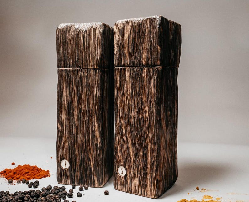May include: A set of two wooden salt and pepper shakers. The shakers are made from dark wood with a natural grain pattern. The shakers are labeled "P" and "S" for pepper and salt.