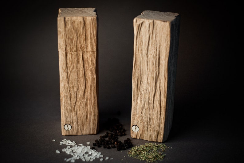 Peut inclure: Deux sali&egrave;res et poivri&egrave;res en bois avec une finition en bois naturel rustique. Les sali&egrave;res sont &eacute;tiquet&eacute;es "S" et "P" et sont pos&eacute;es sur une surface sombre avec du sel, des grains de poivre et des herbes s&eacute;ch&eacute;es.