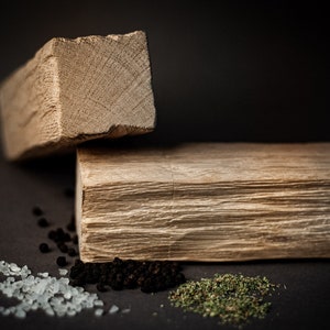 May include: Two wooden blocks, one stacked on the other, against a dark backdrop. Small piles of salt, peppercorns, and dried herbs are scattered around the blocks. The wood has a natural, textured appearance.