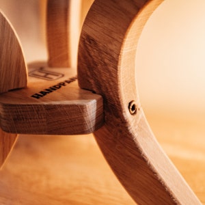 May include: Close-up of a wooden handpan with a brass screw. The handpan is made of light brown wood and has a natural finish. The word "HANDPAN" is engraved on the side of the instrument.