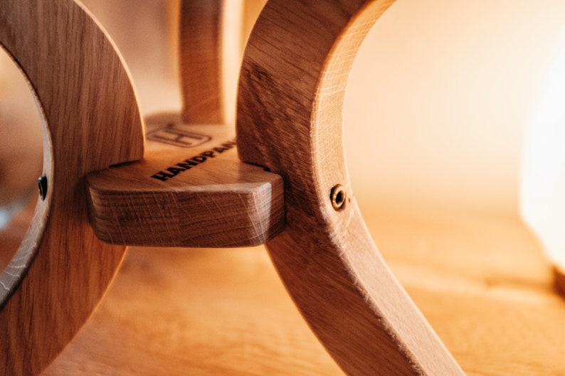 May include: Close-up of a wooden handpan with a brass screw. The handpan is made of light brown wood and has a natural finish. The word "HANDPAN" is engraved on the side of the instrument.
