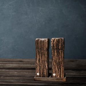 May include: Two wooden salt and pepper shakers with a dark brown wood grain finish. The shakers are sitting on a wooden base.