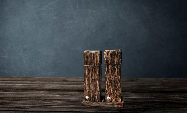 May include: Two wooden salt and pepper shakers with a dark brown wood grain finish. The shakers are sitting on a wooden base.
