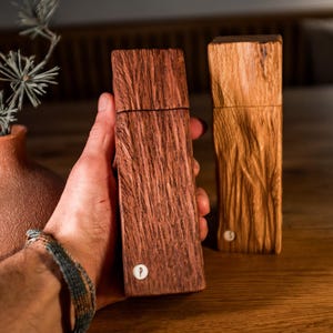 Peut inclure: Deux moulins &agrave; sel et &agrave; poivre en bois, l'un est brun fonc&eacute; avec un motif de grain de bois et l'autre est brun clair avec un motif de grain de bois. Les deux moulins ont un petit bouton en m&eacute;tal sur le dessus.