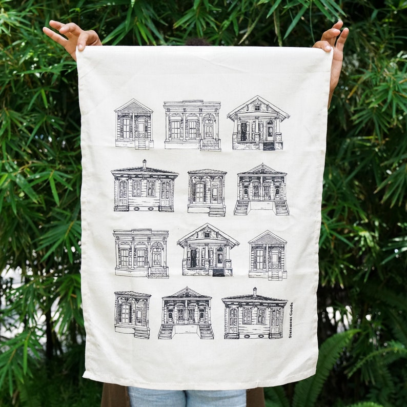 May include: A white kitchen towel with a black and white illustration of 15 different New Orleans style houses. The text "Statement Goods" is printed in the bottom right corner of the towel.