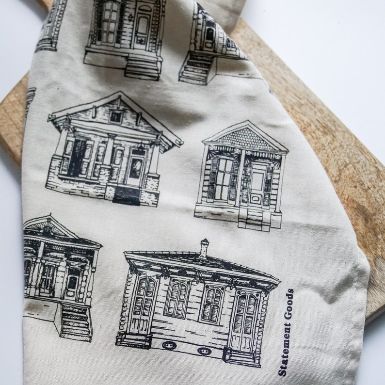 May include: A white tea towel with a black and white print of various house designs. The text "Statement Goods" is printed in the bottom right corner.