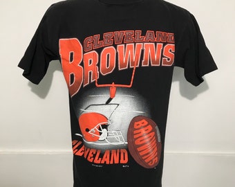 Puede incluir: Camiseta negra con un gráfico vintage de los Cleveland Browns. El gráfico presenta el logotipo del equipo, un balón de fútbol y un casco.