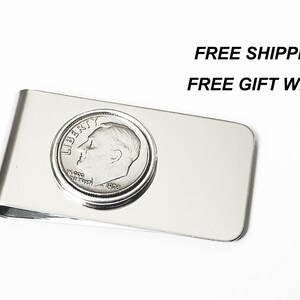 May include: Silver money clip with a dime coin design. The coin features a profile of a man's face with the words "LIBERTY" and "IN GOD WE TRUST".