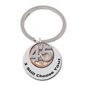 May include: Silver key chain with a round silver charm. The charm has a penny with the number 45 on it and the words "I Still Choose You!" around the edge.
