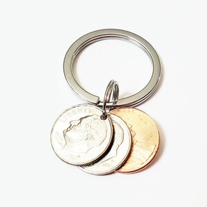 May include: A silver key chain with three coins attached. The coins are a silver dime and two copper pennies. The dime has the profile of a man on it and the pennies have the Lincoln Memorial on them. The coins are dated 2001.
