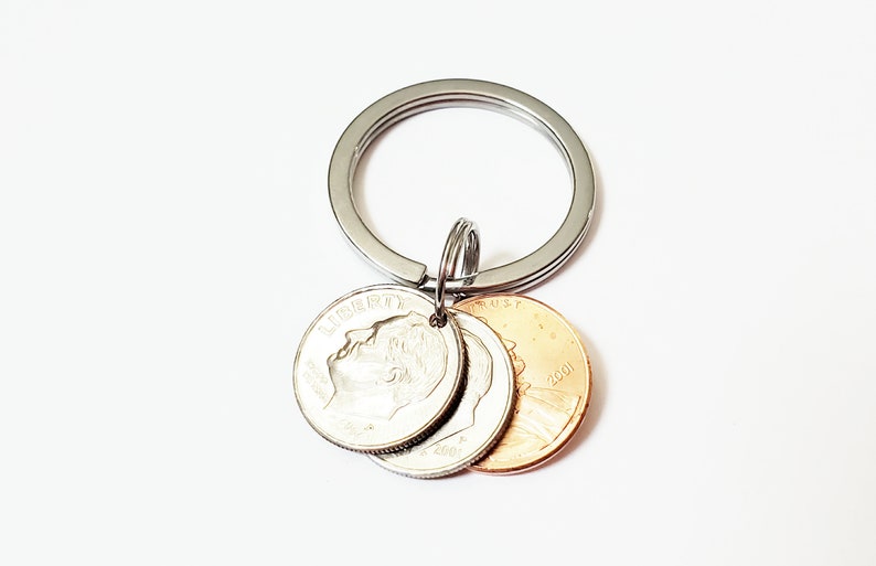 May include: A silver key chain with three coins attached. The coins are a silver dime and two copper pennies. The dime has the profile of a man on it and the pennies have the Lincoln Memorial on them. The coins are dated 2001.