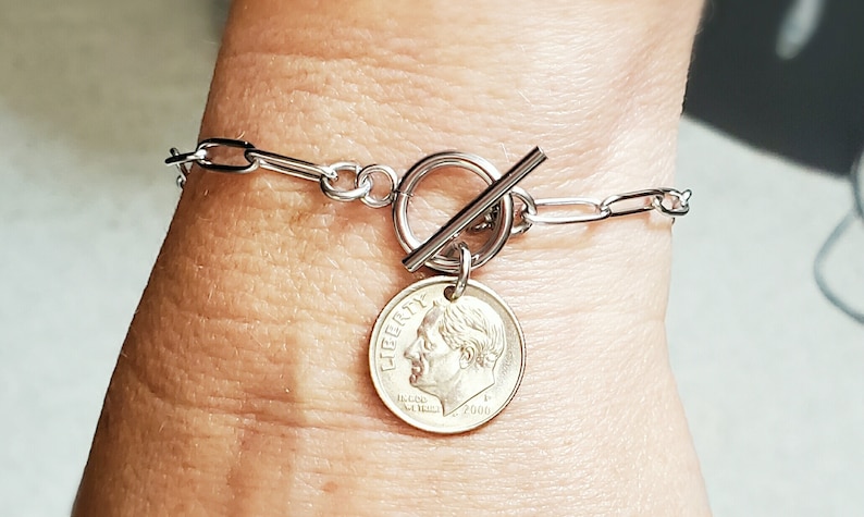 Puede incluir: Un brazalete de cadena de plata con un cierre de palanca y un dije de diez centavos de plata. La moneda de diez centavos est&aacute; fechada en 2000 y presenta el perfil del presidente Franklin D. Roosevelt.