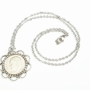 May include: A silver chain necklace with a silver coin pendant. The coin is surrounded by a decorative silver frame.