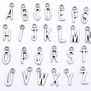 May include: A set of 26 silver-toned metal alphabet letter charms. Each charm features a different letter of the alphabet, from A to Z.