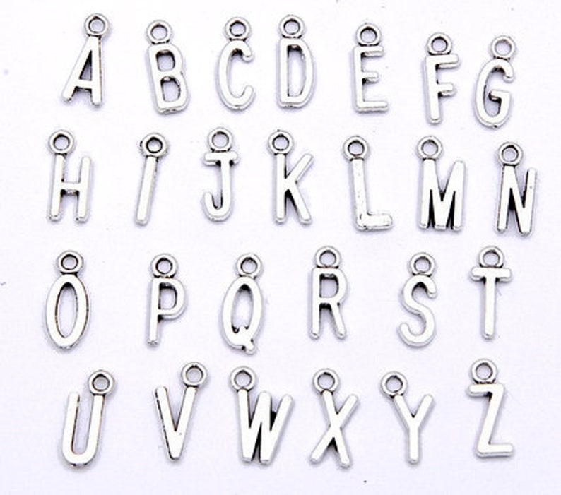 May include: A set of 26 silver-toned metal alphabet letter charms. Each charm features a different letter of the alphabet, from A to Z.