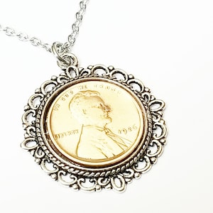 May include: A silver chain necklace with a silver filigree frame pendant featuring a gold-toned 1936 Lincoln penny.