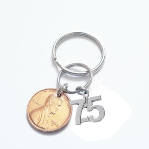 May include: A silver key chain with a penny and a silver charm with the number 75 on it.