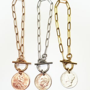 Puede incluir: Tres collares de cadena de oro, plata y oro rosa con cierre de palanca y un colgante de moneda. Las monedas son un centavo estadounidense, una moneda de diez centavos estadounidense y un n&iacute;quel estadounidense.