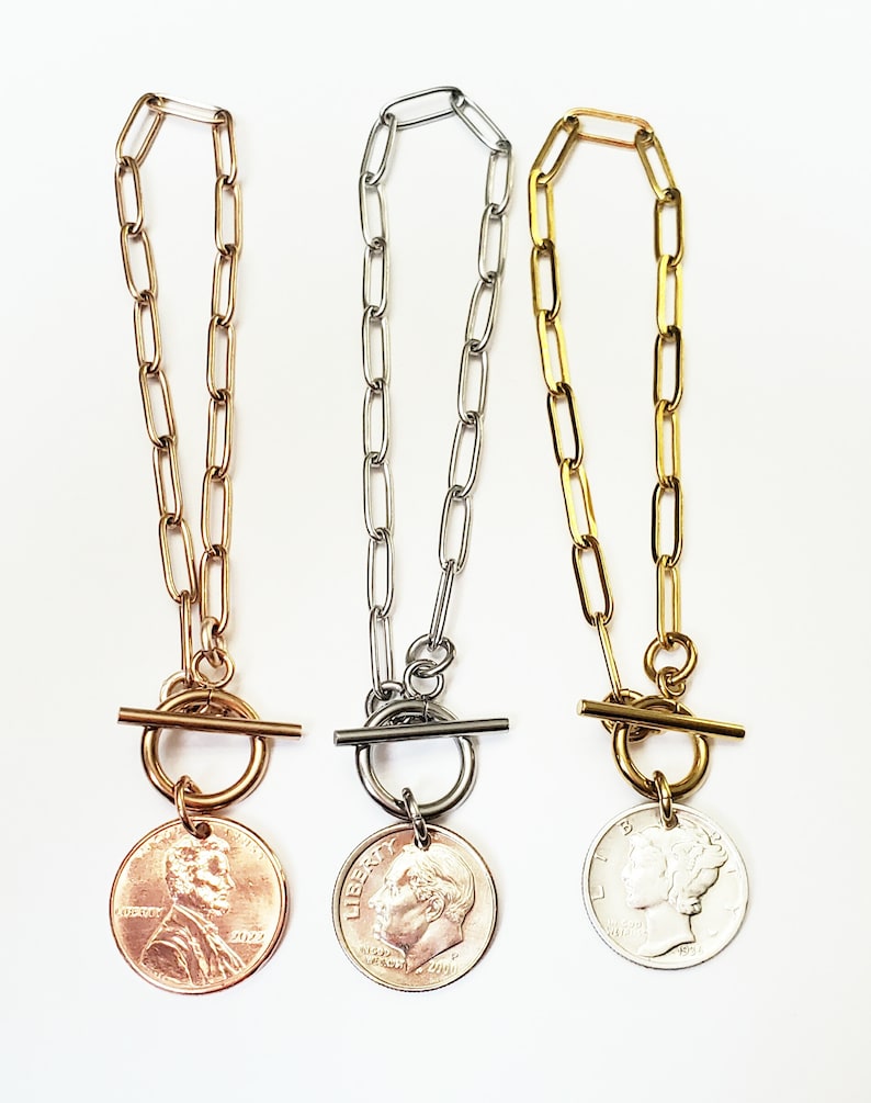 Puede incluir: Tres collares de cadena de oro, plata y oro rosa con cierre de palanca y un colgante de moneda. Las monedas son un centavo estadounidense, una moneda de diez centavos estadounidense y un n&iacute;quel estadounidense.