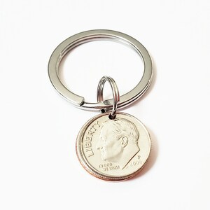 May include: A silver key chain with a silver dime charm. The dime is dated 2000 and has the words "LIBERTY" and "IN GOD WE TRUST" inscribed on it.