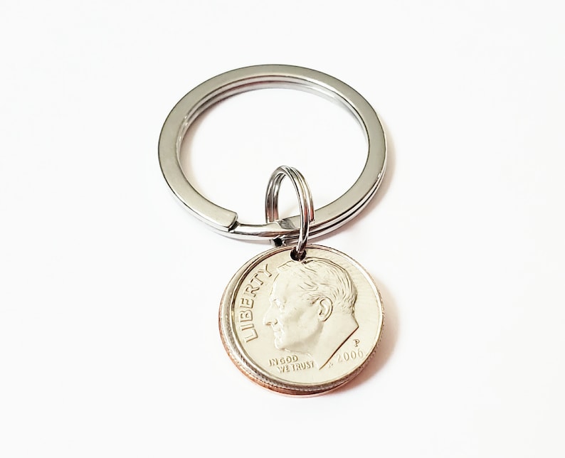 May include: A silver key chain with a silver dime charm. The dime is dated 2000 and has the words "LIBERTY" and "IN GOD WE TRUST" inscribed on it.