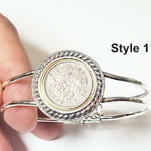 May include: Silver bangle bracelet with a silver and gold coin charm featuring a sixpence coin with the inscription "SIXPENCE" and the year "1969". The bracelet is labeled "Style 1".