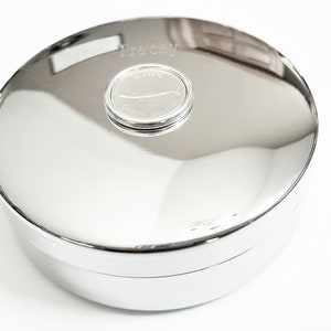 May include: A silver round box with a lid. The lid has a small round silver plate with the name "Tracey" engraved on it.