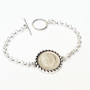 May include: A silver chain bracelet with a silver dime coin charm. The coin features a profile of Abraham Lincoln and the inscription "LIBERTY".