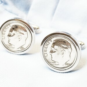 May include: A pair of silver cufflinks featuring a silver coin with the profile of Abraham Lincoln and the words "LIBERTY" and "IN GOD WE TRUST".