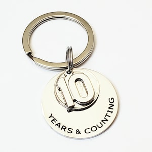 May include: Silver keychain with a round charm that says "10 Years & Counting" with a smaller charm featuring the number 10.