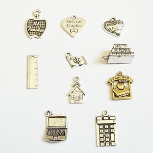 May include: Assortment of silver and gold charm pendants with teacher-themed designs, including an apple, a heart, a book, a ruler, a schoolhouse, a calculator, a laptop, and a stack of books with the words "Math, Science, History".