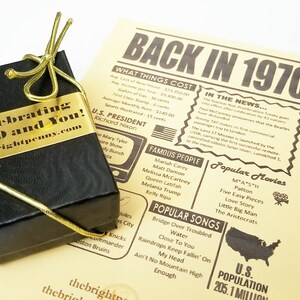May include: A black gift box with a gold ribbon and a gold label that says "Celebrating 1970 and You! thebrightpenny.com". The box is sitting on a yellow paper with a newspaper-style design that says "Back in 1970" and lists events, famous people, and popular movies from the year 1970.