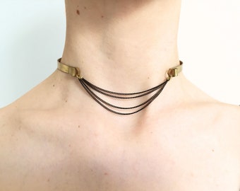 May include: A gold choker necklace with multiple black chains hanging from it.