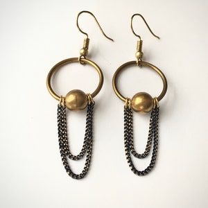 May include: Gold hoop earrings with a dangling chain and a gold bead. The chain is made of two different types of metal, one gold and one black.