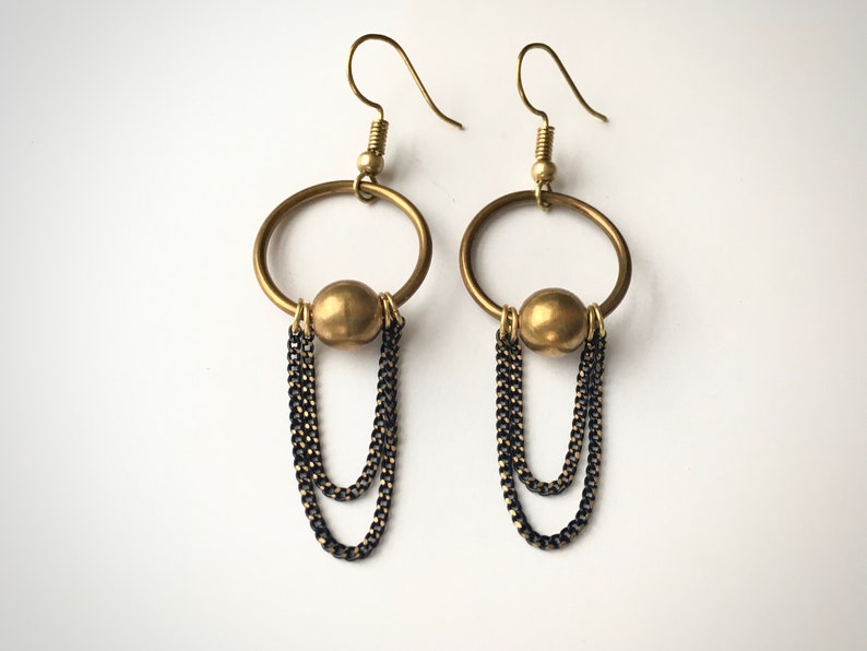 May include: Gold hoop earrings with a dangling chain and a gold bead. The chain is made of two different types of metal, one gold and one black.