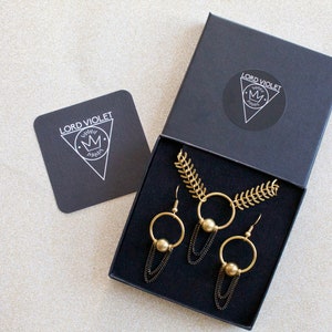 May include: A black box with a gold necklace and earrings. The box has the logo "LORD VIOLET" with a crown on it.