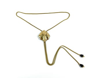 May include: A gold chain necklace with a large, gold, shell-shaped pendant and black bead accents at the ends.