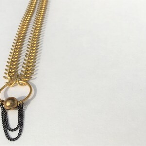 May include: A gold chain necklace with a large, round, gold pendant. The pendant has a smaller, round, gold bead hanging from it. The chain is made of small, linked, gold pieces.