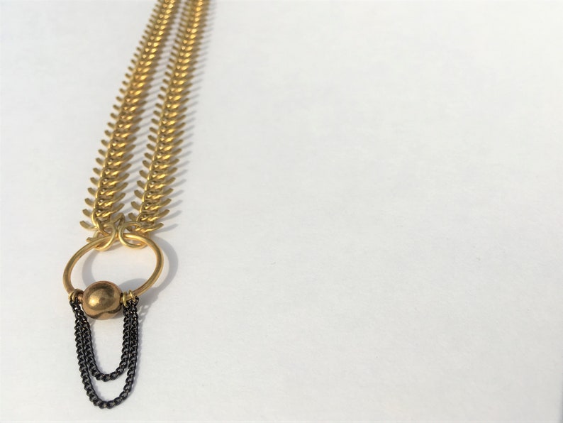 May include: A gold chain necklace with a large, round, gold pendant. The pendant has a smaller, round, gold bead hanging from it. The chain is made of small, linked, gold pieces.