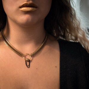 May include: A gold chain choker necklace with a small round pendant and a black chain hanging from it.